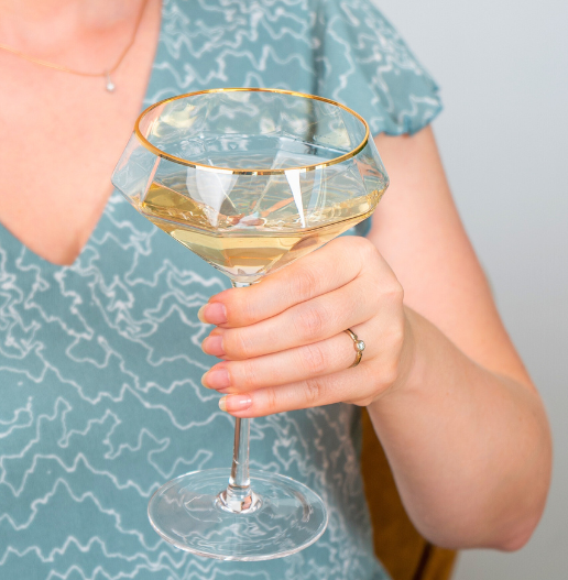 martini coupe glasses diamond shape long stem in a hand of a woman warm light